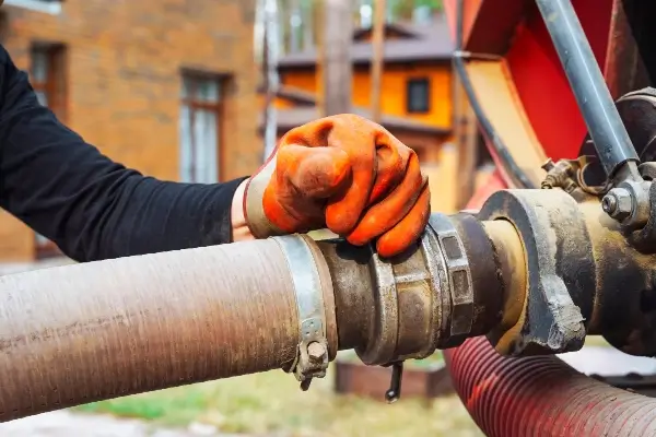 A septic worker wearing gloves connects a septic hose to a truck in the process of emptying a septic tank. If your septic alarm is going off, you need help from a septic service professional.