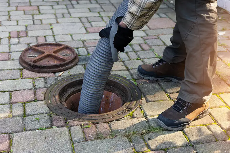 A worker placing a septic hose into a septic tank. Professional septic tank care and maintenance is vital for all buildings with a septic system.