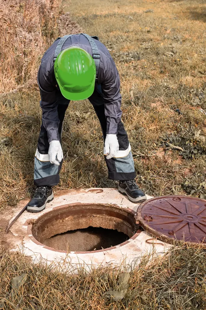 A worker in protective gear examines an open septic tank outdoors. Routine inspections like this can ensure the longevity of your septic system. Schedule a service with Puget Sound Septic to keep your system running smoothly.